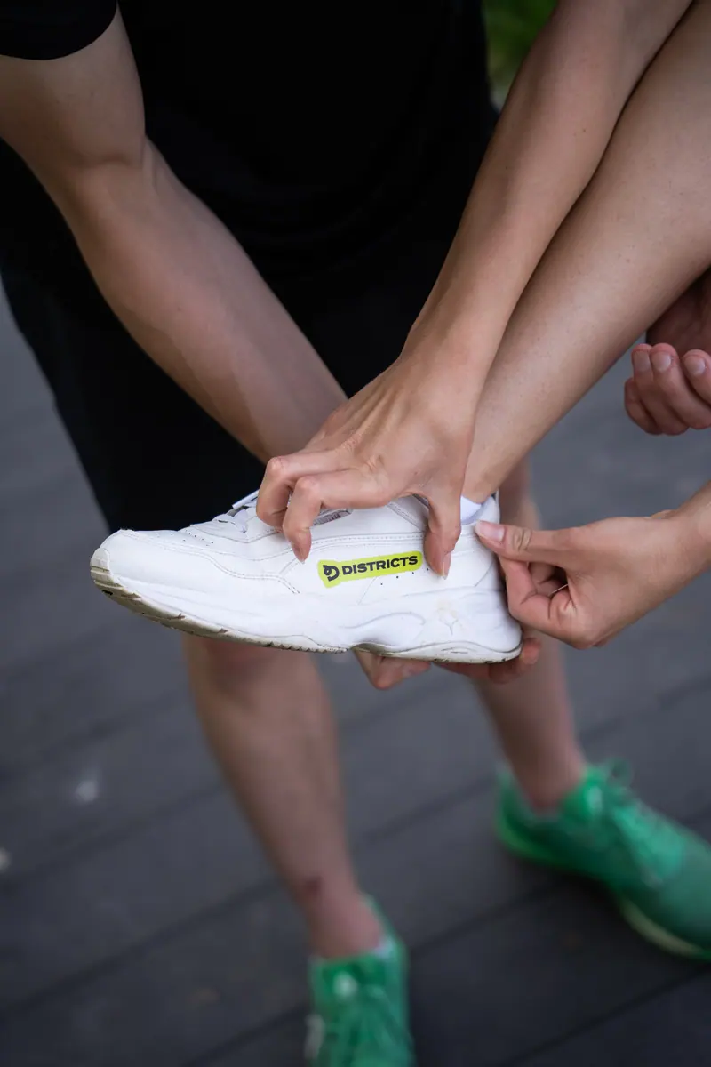 Dłonie przyklejają naklejkę Districts na biały sneakers